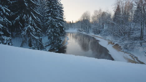 revealing motion shot of river by snowy forest in wintertime finland