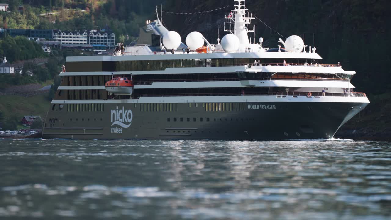 A large cruise liner leaves the port in the eGeiranger fjord and moves slowly along the fjord.