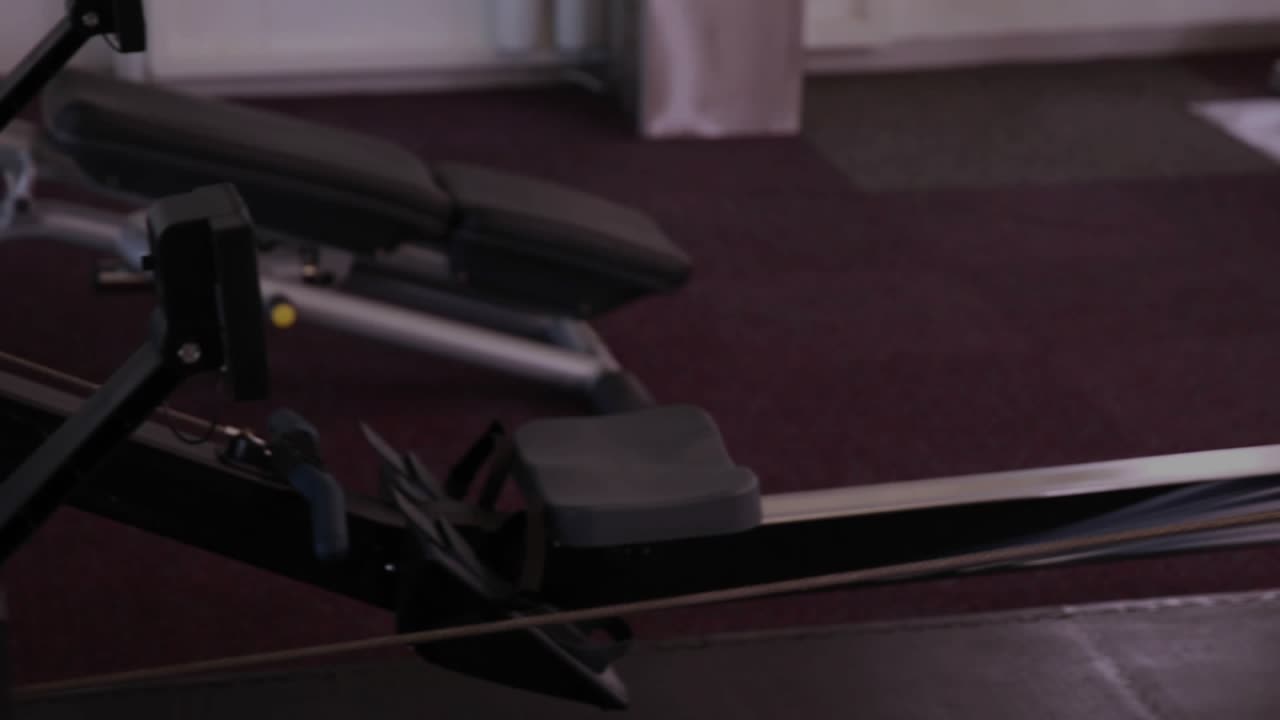 Adult woman initiating rowing drive after catch in gym, HUD graphs tracking power for training