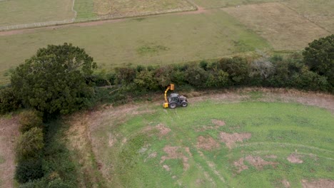 aerial tracking view of tractor cutting and maintaining hedge in field