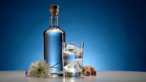 still life with water bottle, glass of ice water, and flowers on a blue background