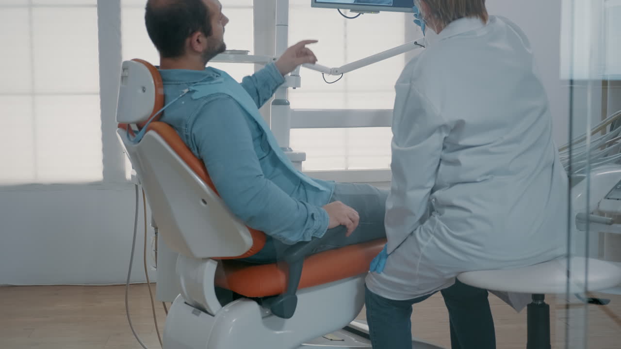 dentista maduro apuntando a la radiografía de los dientes en el monitor