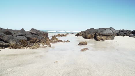 Waves-trickling-in-between-black-lava-rocks-in-a-pristine-beach