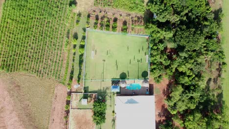 Draufsicht-Auf-Ein-Sommerhaus-Mit-Menschen,-Die-Auf-Der-Grünen-Wiese-Fußball-Spielen