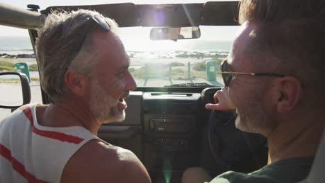 happy caucasian gay male couple driving car and talking on sunny day at the beach