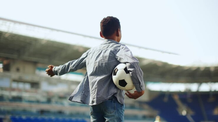 niño sosteniendo una pelota de fútbol en un estadio