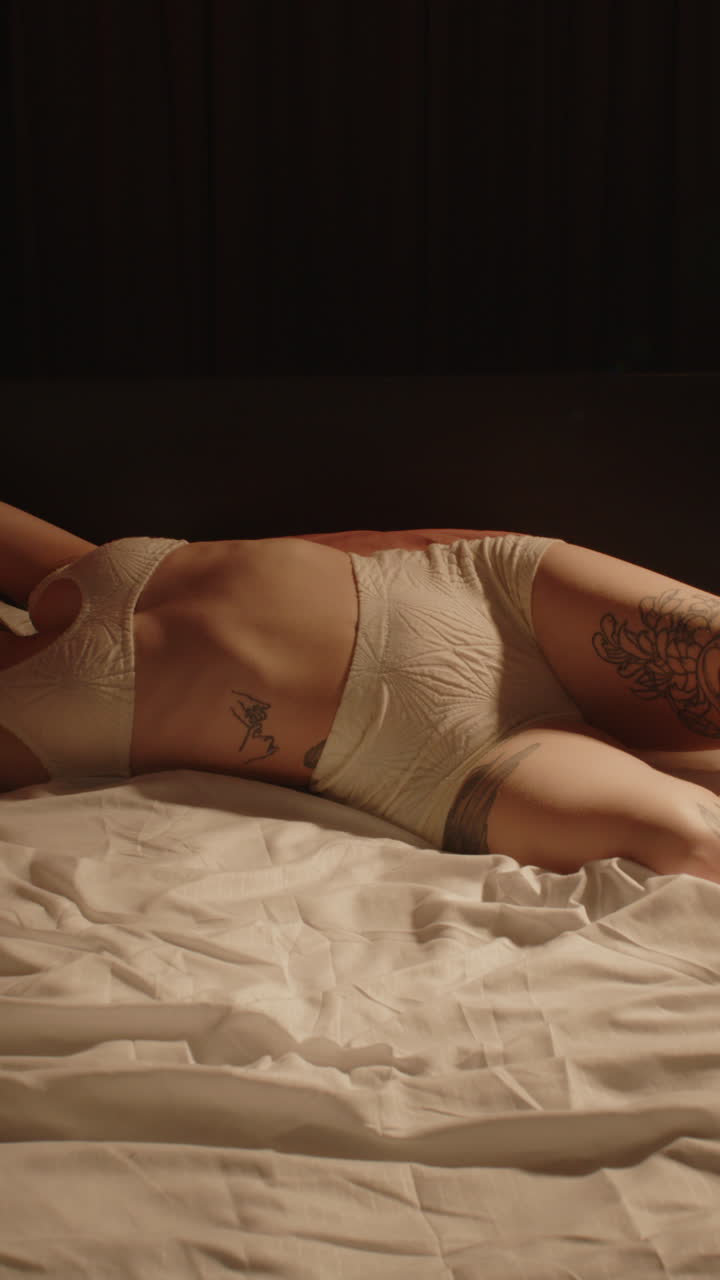 Splendido primo piano verticale dei fianchi di una bella donna che indossa lingerie di lana mentre si gira su un fianco nel letto.