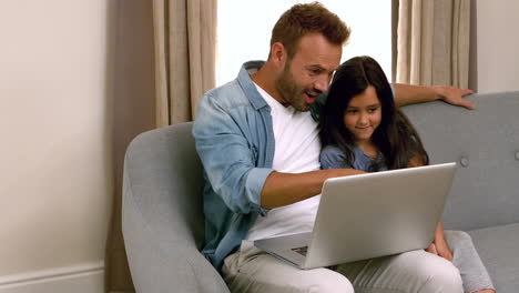 padre y hija felices usando la computadora portátil en el sofá