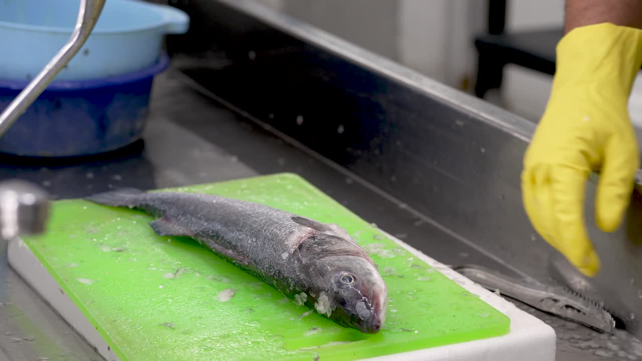 In a vibrant kitchen setting, a skilled chef clad in yellow gloves expertly fillets a fresh catch. Brightly colored platters surround him, showcasing the culinary artistry of Japanese cuisine