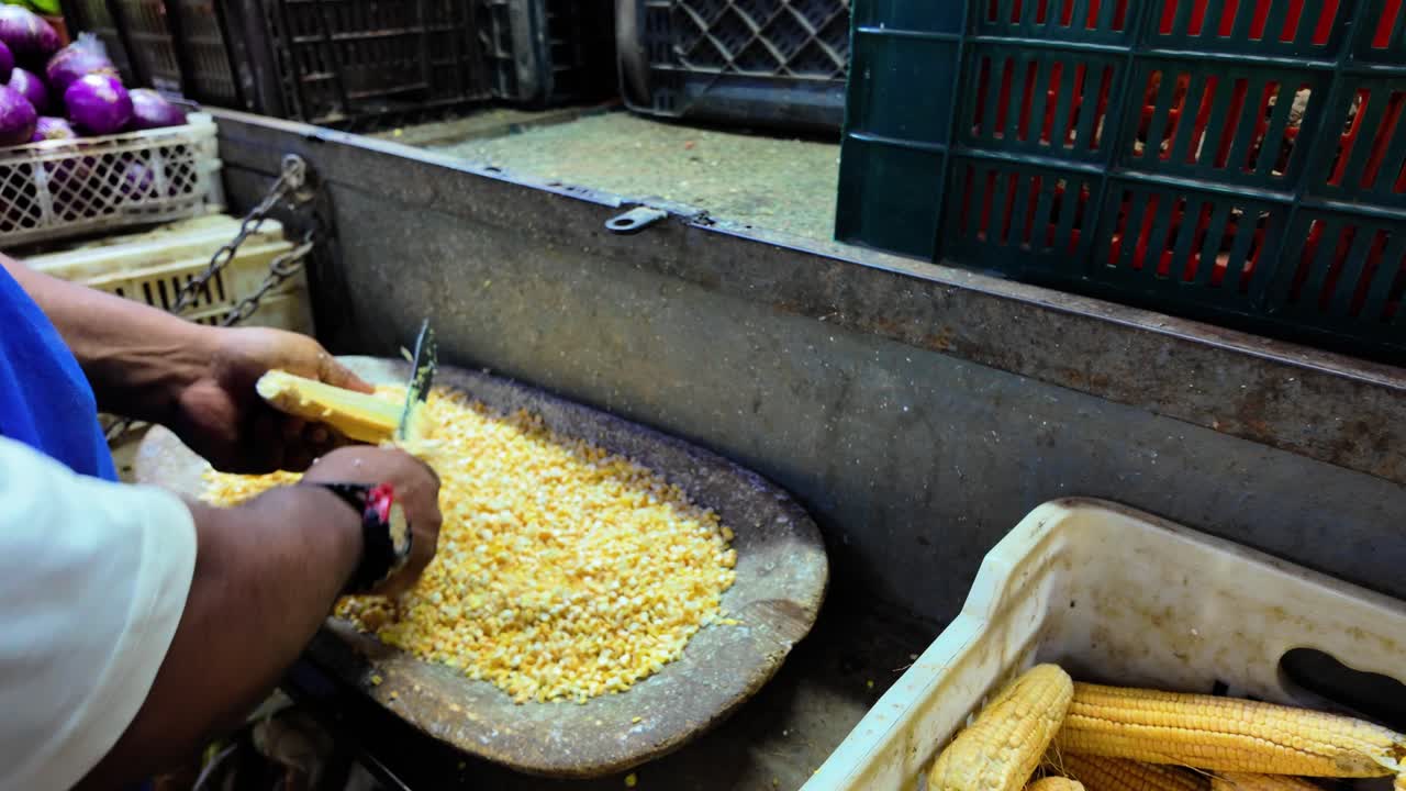 Hand showing how to remove corn kernels from cob in a market setting