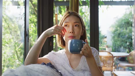 asian woman drinking coffee and lying on couch