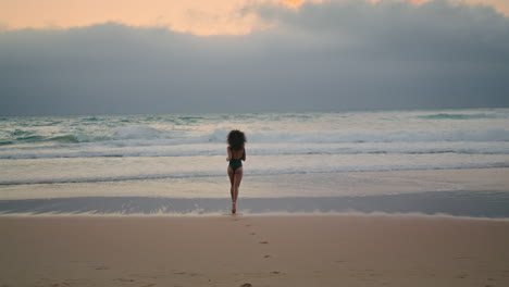 back view woman running to ocean waves summer evening in distance. girl jogging.