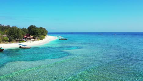 Crystal-emerald-water-of-turquoise-lagoon-washing-tranquil-exotic-beach-with-white-sand-on-tropical-island,-anchored-boats-waiting-for-tourists-in-Myanmar