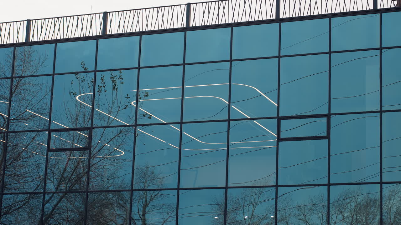 Glass decoration of fitness center reflecting surrounding trees while interior lights glow through panels, blending outdoor nature with modern architecture in striking mirrored facade