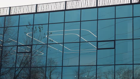 glass decoration of fitness center reflecting surrounding trees while interior lights glow through panels, blending outdoor nature with modern architecture in striking mirrored facade