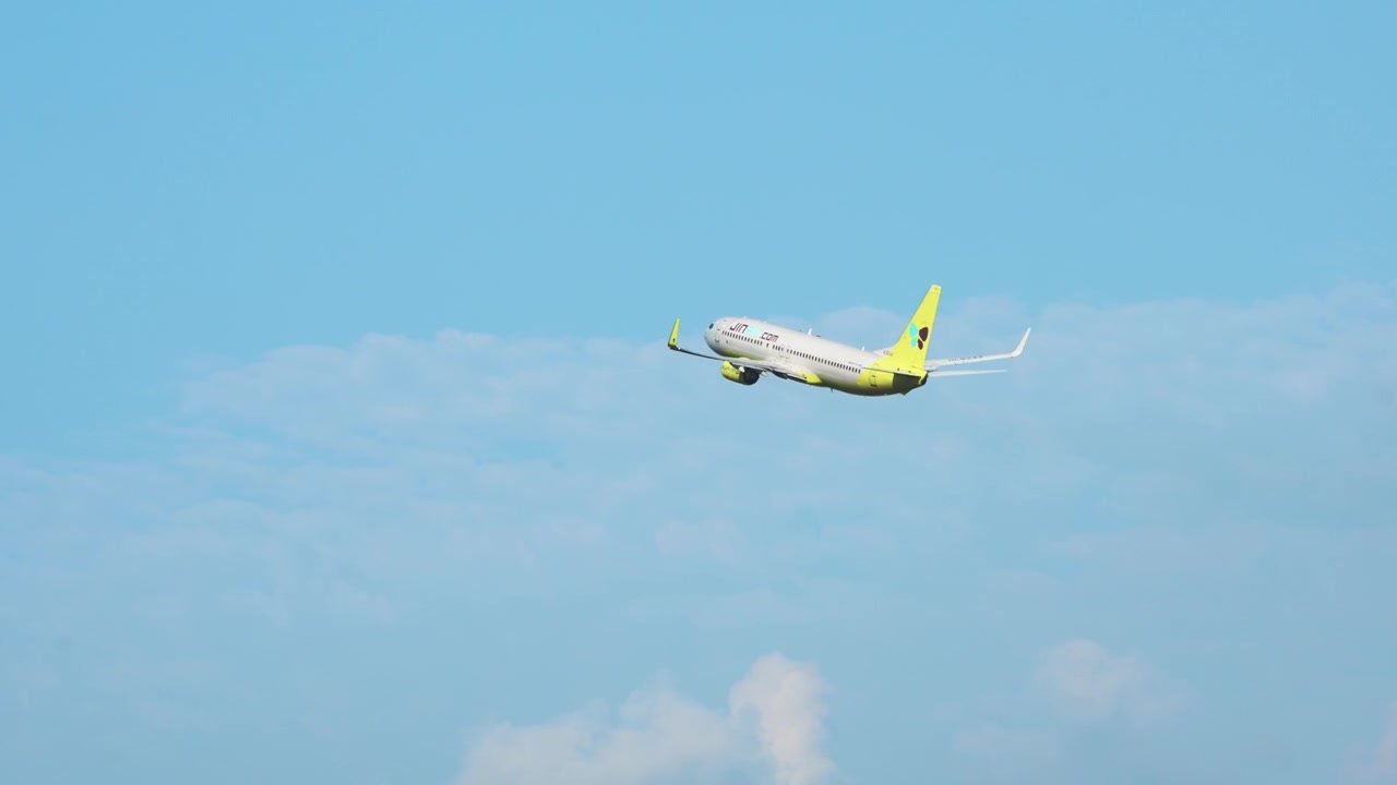 Jin Airs gul- og hvitfargede Boeing 737 passasjerfly klatrer bratt etter avgang, sporet over lys blå himmel over Sør-Korea