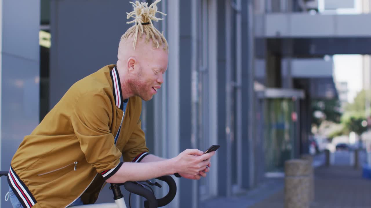 Happy albino african american man with dreadlocks on bike using smartphone