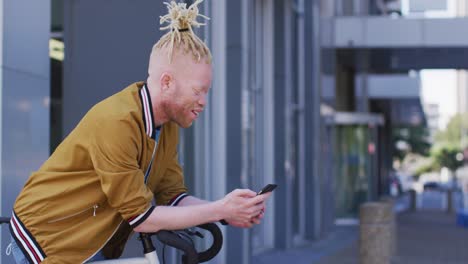 happy albino african american man with dreadlocks on bike using smartphone