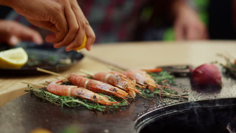 Unknown-person-squeezing-lemon-on-shrimp-outdoors.-Prawns-browning-with-herbs