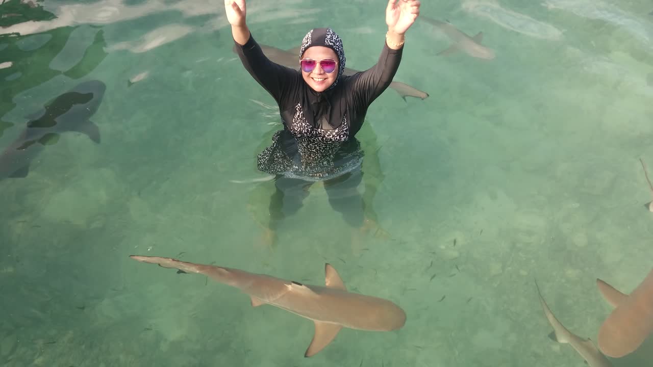 una turista con gafas divirtiéndose con tiburones bebés nadando a su alrededor