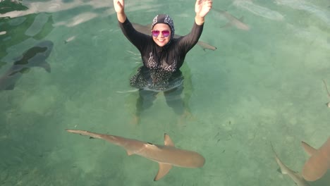 a female tourist wearing glasses having fun with baby sharks swimming around her