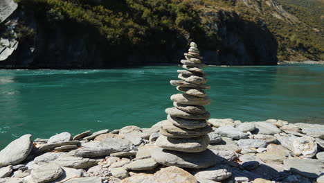 Cairn-or-man-made-stack-of-stones-along-the-riverbank-of-the-Kawarau-River,-New-Zealand---low-angle-parallax