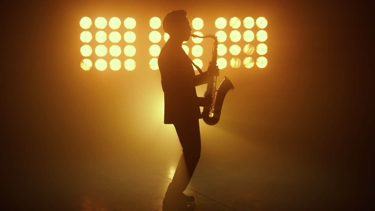 스포트라이트에서 색소폰을 연주하는 실루 재즈 뮤지션. 멜로디를 연주하는 남자.