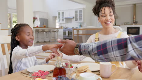 felices padres afroamericanos y su hija orando antes del desayuno en casa, en cámara lenta.