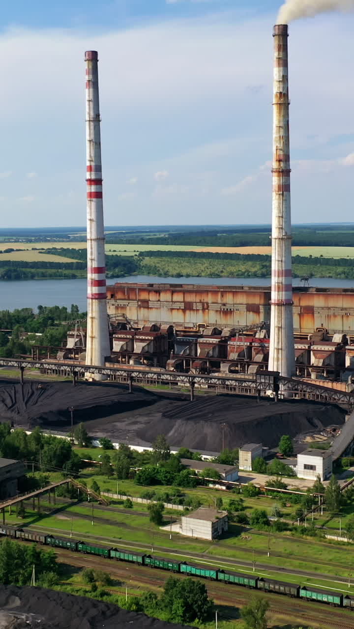 Chemical plant with smoking pipe. Industrial factory among green nature. Pollution of the environment. Aerial view. Vertical video