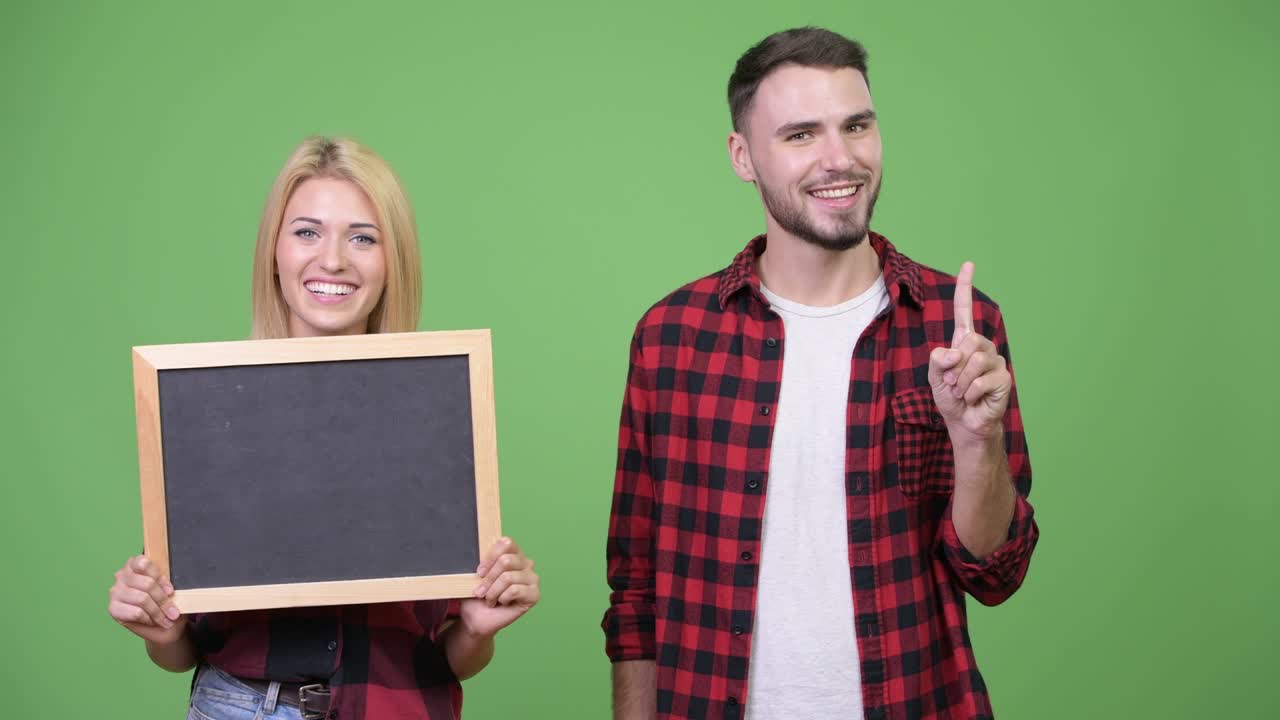 Young couple holding blackboard and pointing finger up together