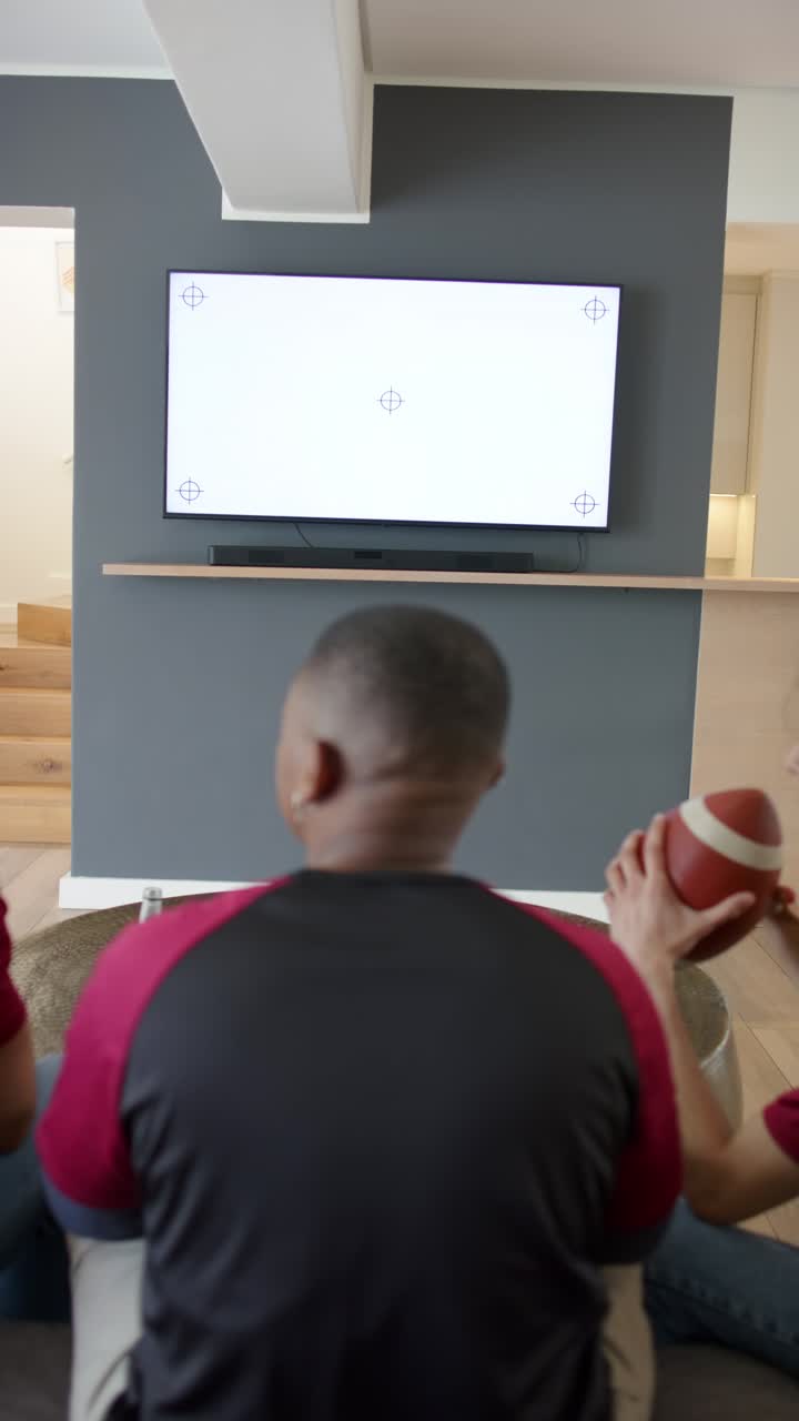 Video verticale: uomini diversi su un divano con un pallone e una bevanda che guardano la TV mentre un uomo entra a sinistra