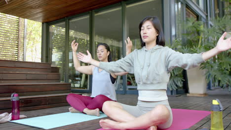 Amigas-Asiáticas-Enfocadas-Practicando-Meditación-De-Yoga-En-Una-Terraza-Soleada,-Cámara-Lenta