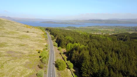 Car-driving-along-scenic-road-with-forest-and-lake-Lomond-in-background,-Scotland