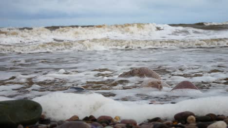 foamy breaking ocean surf pebble beach shoreline tide soothing multicoloured stones closeup left dolly