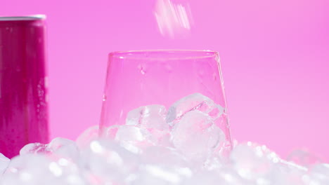 Nahaufnahme-Einer-Person,-Die-Gekühltes-Kaltgetränk-Aus-Der-Dose-Auf-Eiswürfeln-Vor-Rosa-Hintergrund-In-Ein-Glas-Gießt