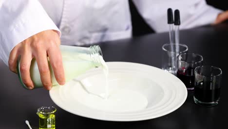una persona con una bata de laboratorio vierte leche en un plato, rodeada de equipo científico, en un entorno controlado