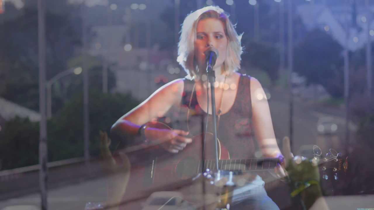 Teen musician singing at mic playing guitar on stage with street lamp reflections for entertainment