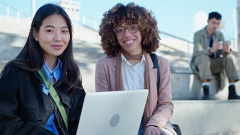 young cheerful women sitting with laptop outside and posing at camera
