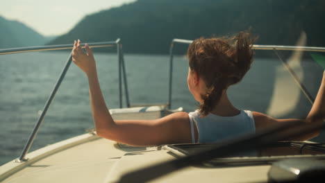 joven mujer positiva endereza el cabello mirando fuera de la escotilla de un barco de motor moderno. moviéndose a lo largo del mar con una vista pintoresca de la belleza de la naturaleza en un clima soleado