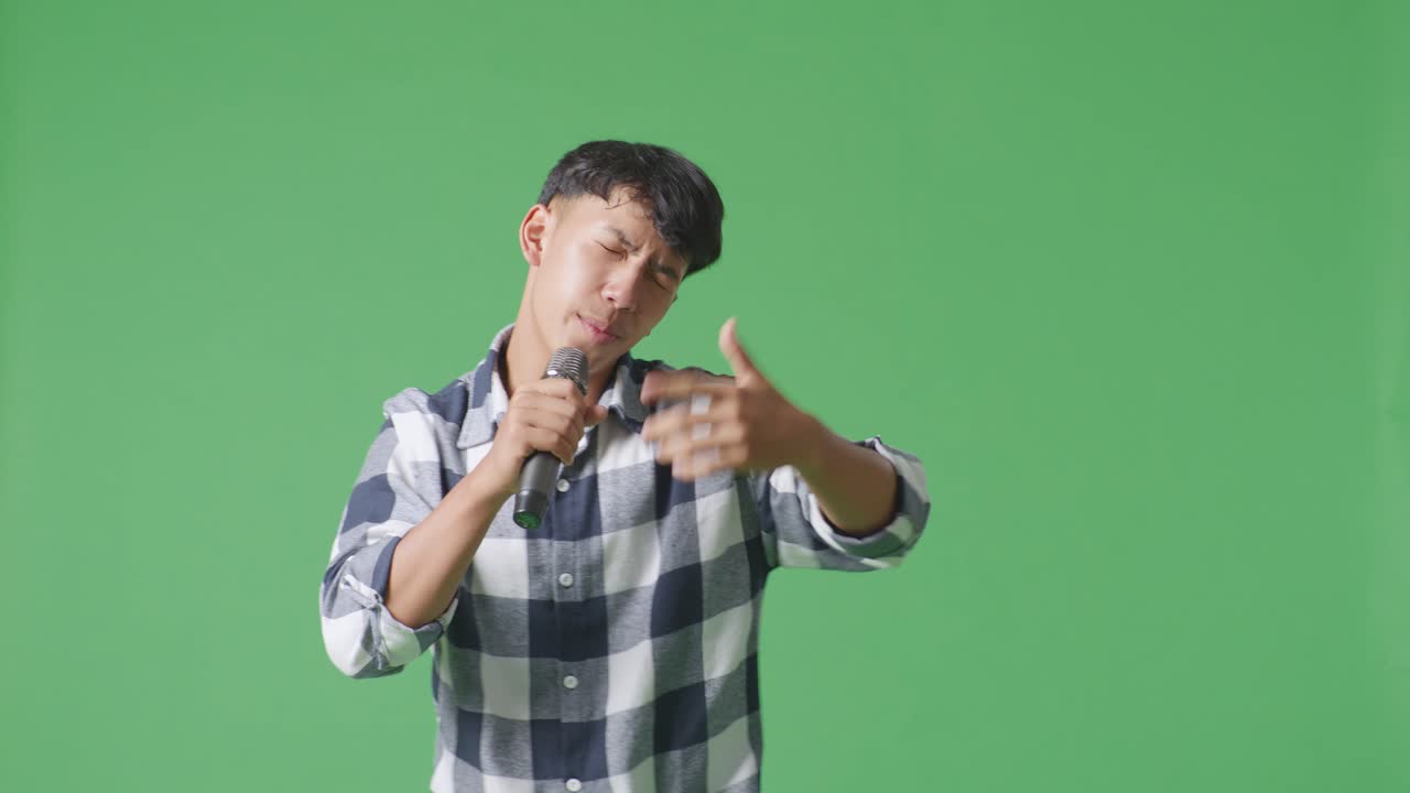 젊은 아시아 십대 소년이 마이크를 들고 녹색 화면 배경에서 을 연주하고 있습니다.
