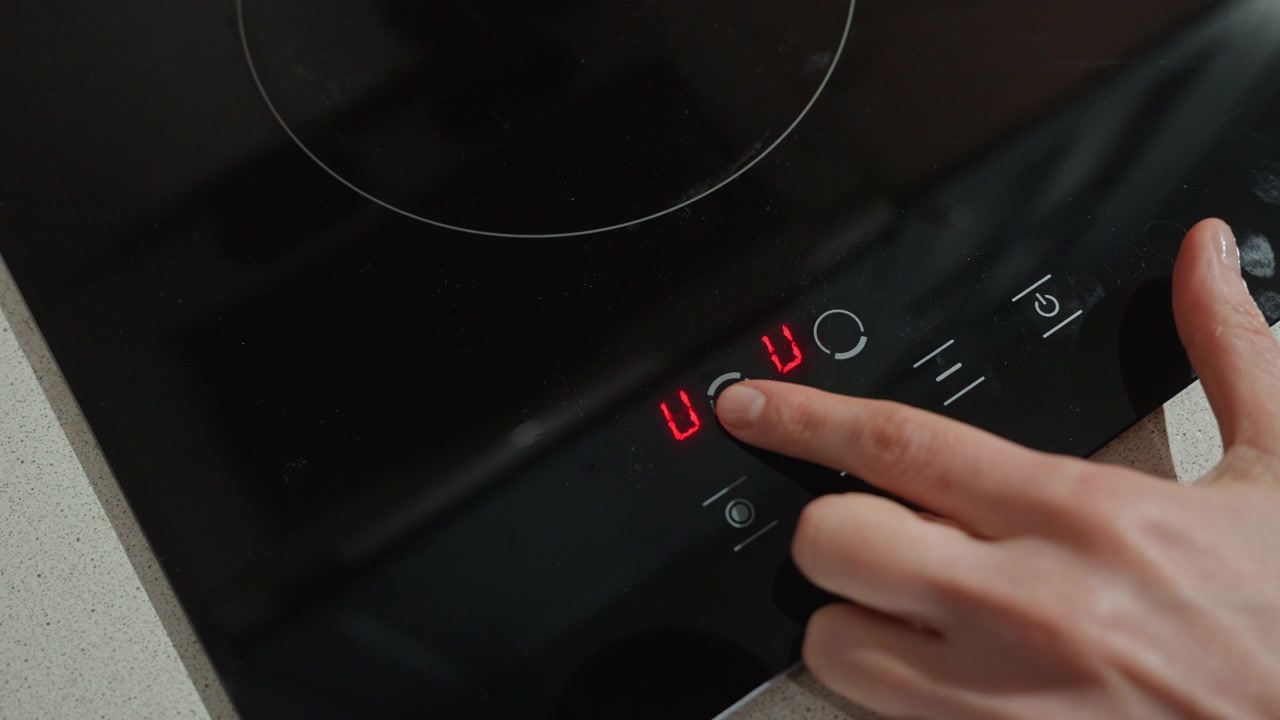 Primo piano del controllo di un piano cottura a induzione in cucina, mano che regola il timer digitale e le impostazioni di calore su un elegante piano cottura nero con display rosso luminoso, tranquilla atmosfera domestica mattutina, pressione attenta del dito sul touch