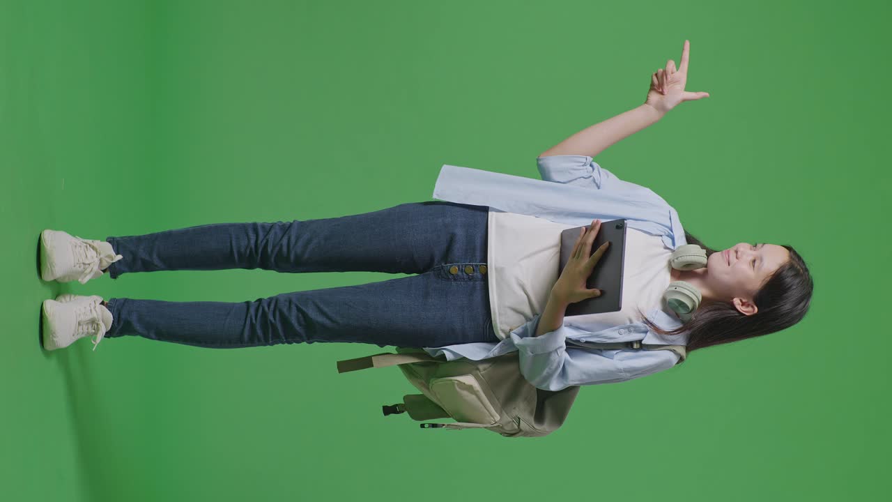 녹색 화면 배경 스튜디오에 서있는 동안 태블릿을 사용하고 으로 가리키는 배을 가진 아시아 십대 소녀 학생의 전체 몸