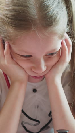 little girl in bad mood leans face on hands sitting with junior brother in home classroom closeup. bored sister and toddler kid at domestic lesson