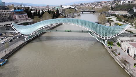 Aerial-shot-of-peace-bridge-Georgia-Tbilisi-city-center-river-cars-people-old-buildings