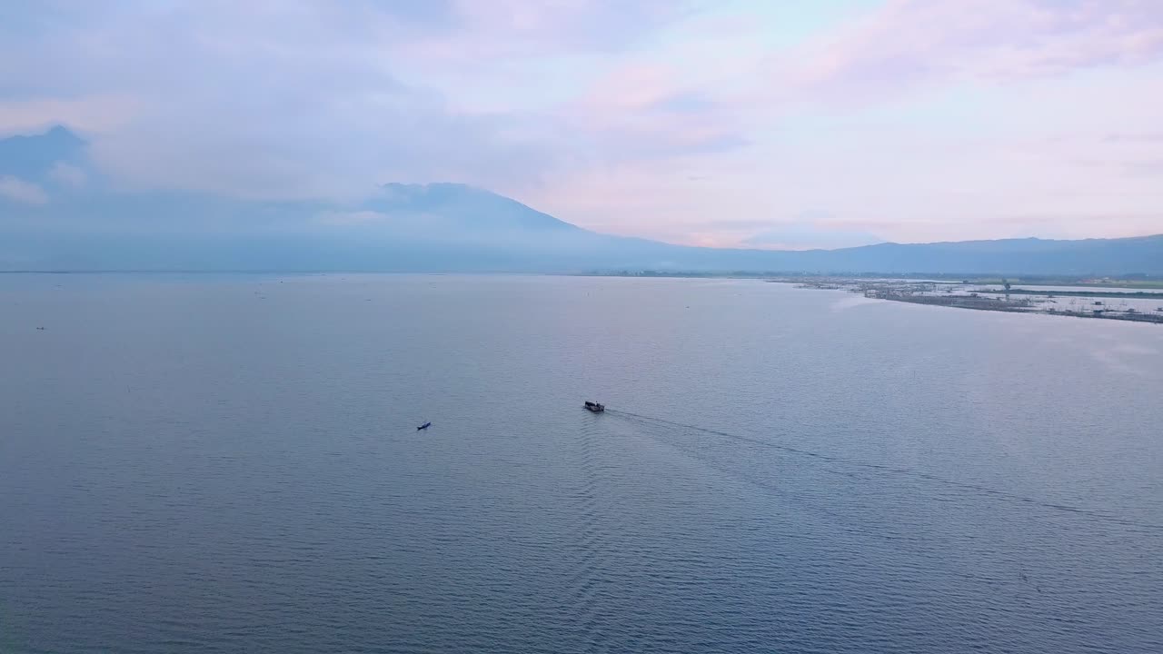 산과 해안을 배경으로 인도네시아의 라와 호수에서 카누를 지나는 어선