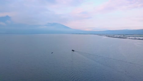 Fischerboot-Vorbei-An-Kanu-Auf-Dem-Rawa-See-Pening-In-Indonesien-Mit-Bergen-Und-Ufer-Im-Hintergrund