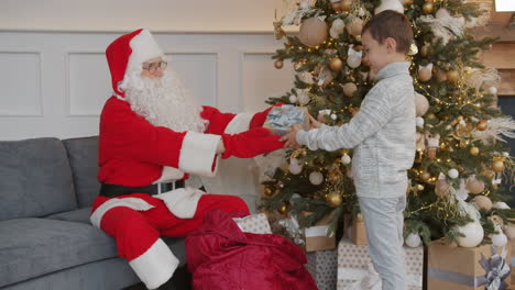 santa giving a gift to a child by a christmas tree