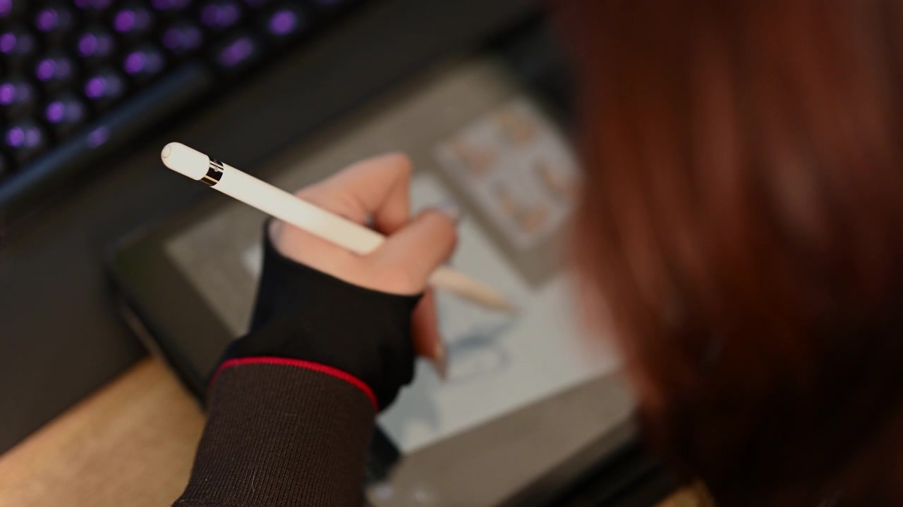 学生が白いスタイラスペンを使って、デジタル描画タブレットにシンプルなキャラクターのスケッチを描いているクローズアップ。