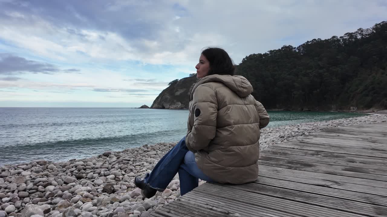 Person sitting alone on a quiet sandy beach facing the ocean