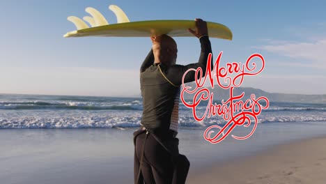 Animation-of-merry-christmas-over-african-american-senior-man-with-surfboard-on-beach